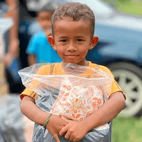 A kid receiving a school bag filled with school supplies from KSK's School Mission programme