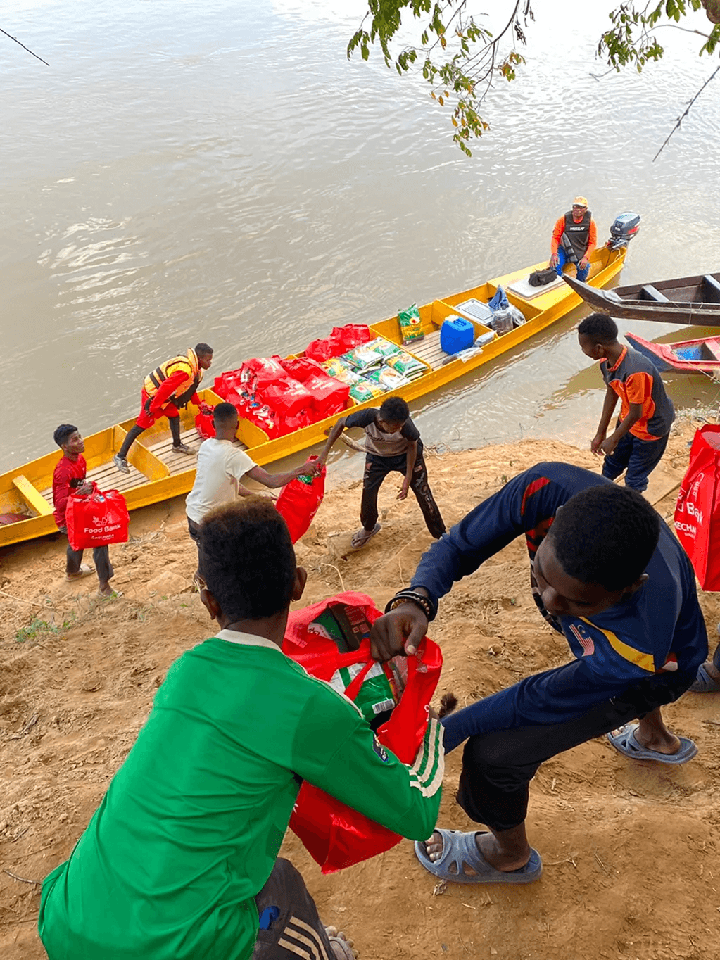 Orang Asli passing food package from a boat to a family on the riverbank